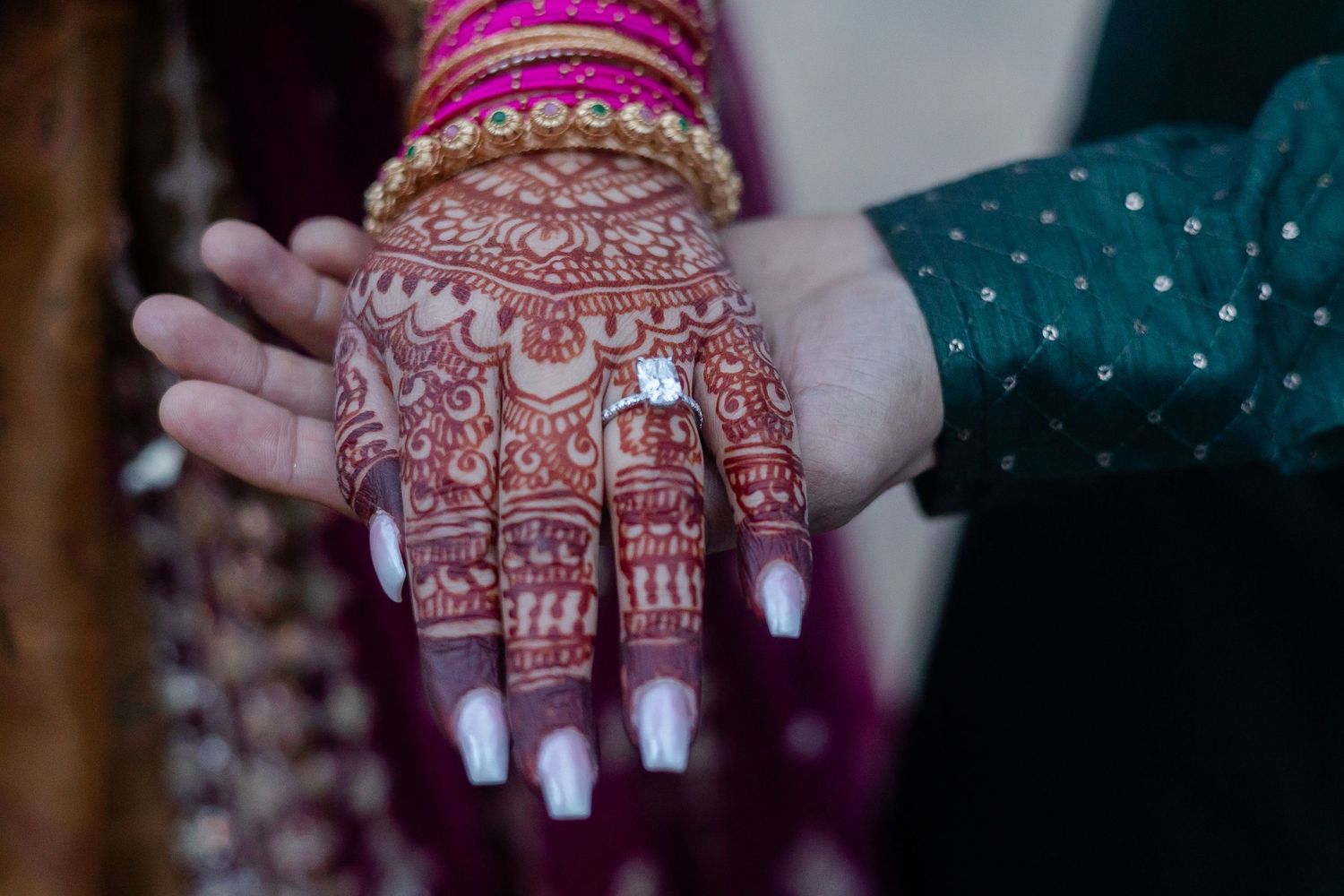 Close-up of intricate henna designs on hands with white nail polish.