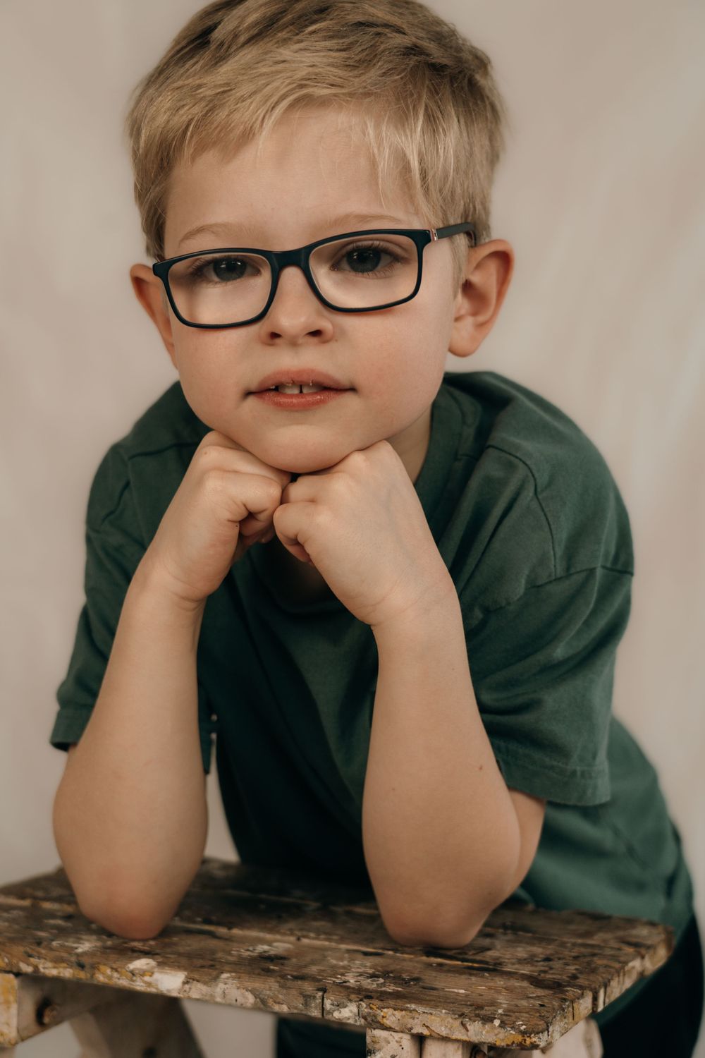 A boy leaning on wooden step with his chin resting on his hands looking into the camera.