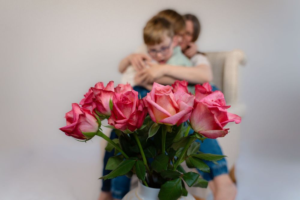 A mother and her children hugging with a beautiful bunch of roses in the foreground.