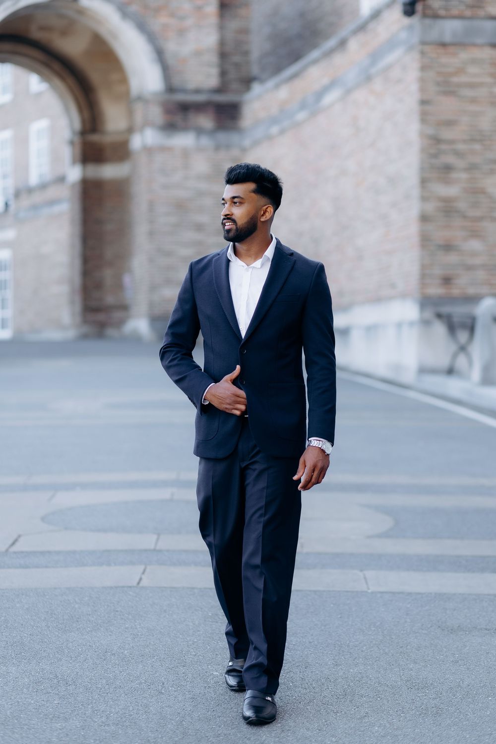 Professional wearing a dark suit walks confidently through an urban setting with brick archways in the background.