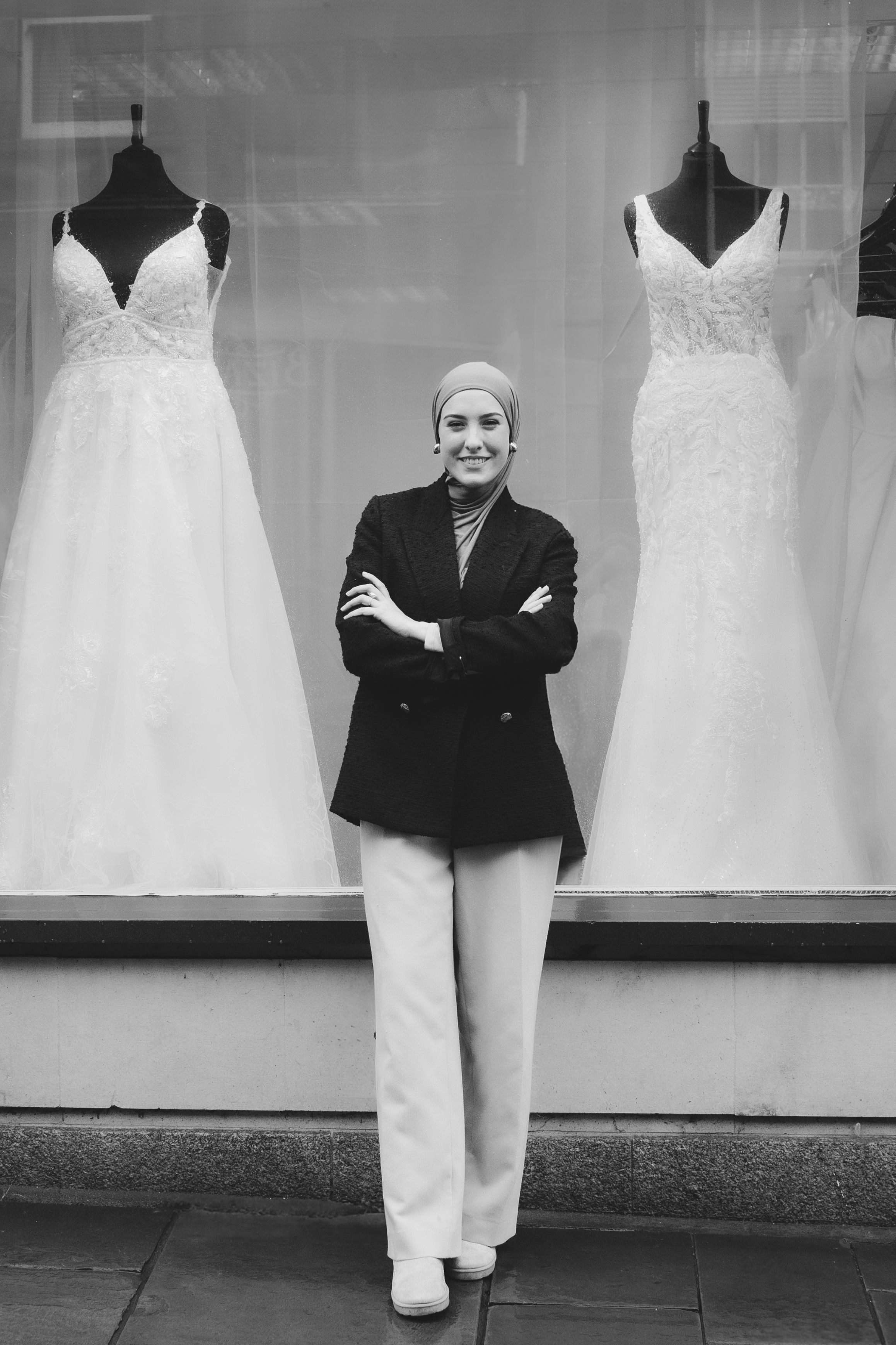 A black and white photo showing a bridal shop window display with elegant white wedding dresses on mannequins.