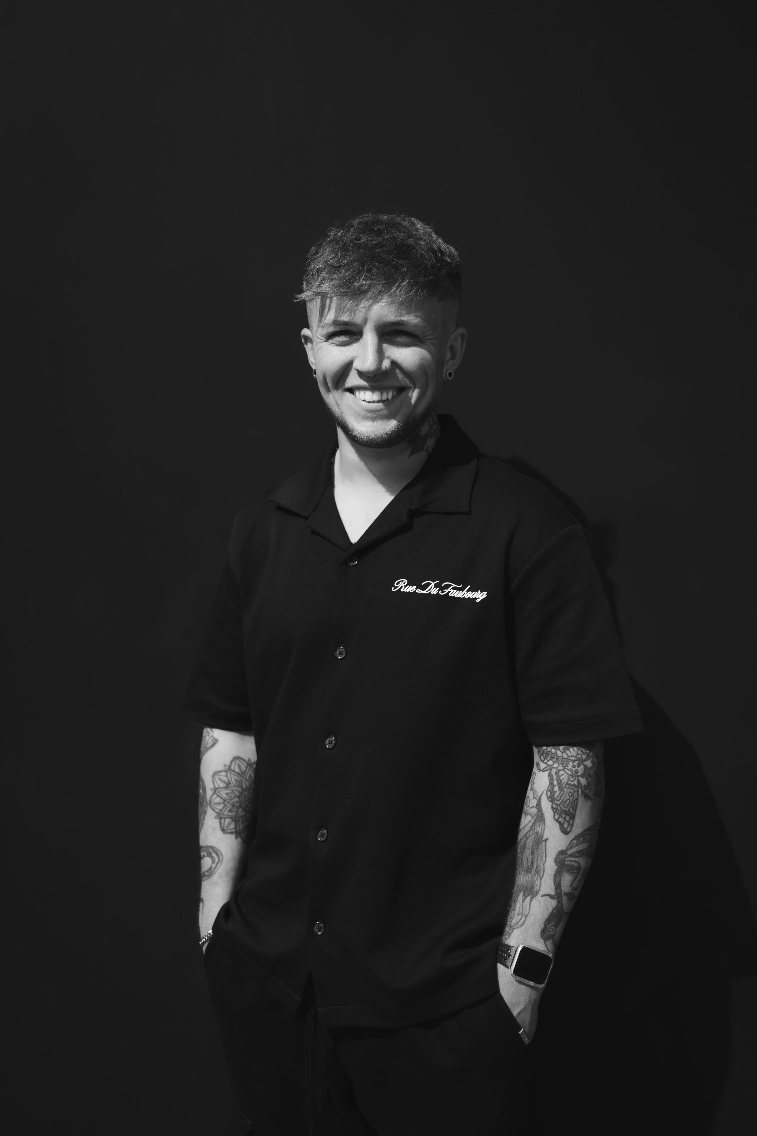 Black and white portrait series showing someone in dark clothing with visible tattoos against a dark background.