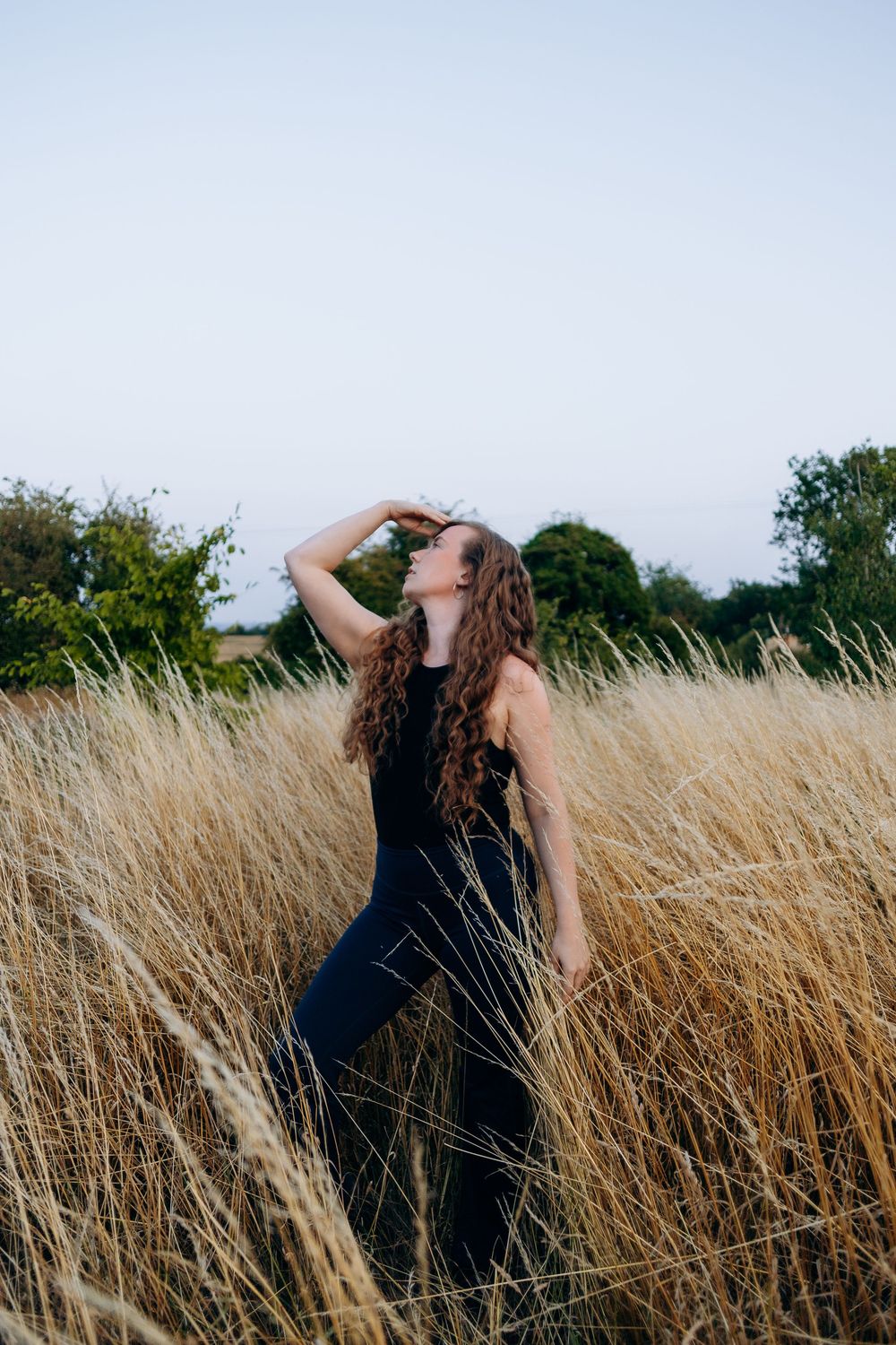 A figure stands in golden tall grass, arching backward in a flowing movement sequence at sunset.