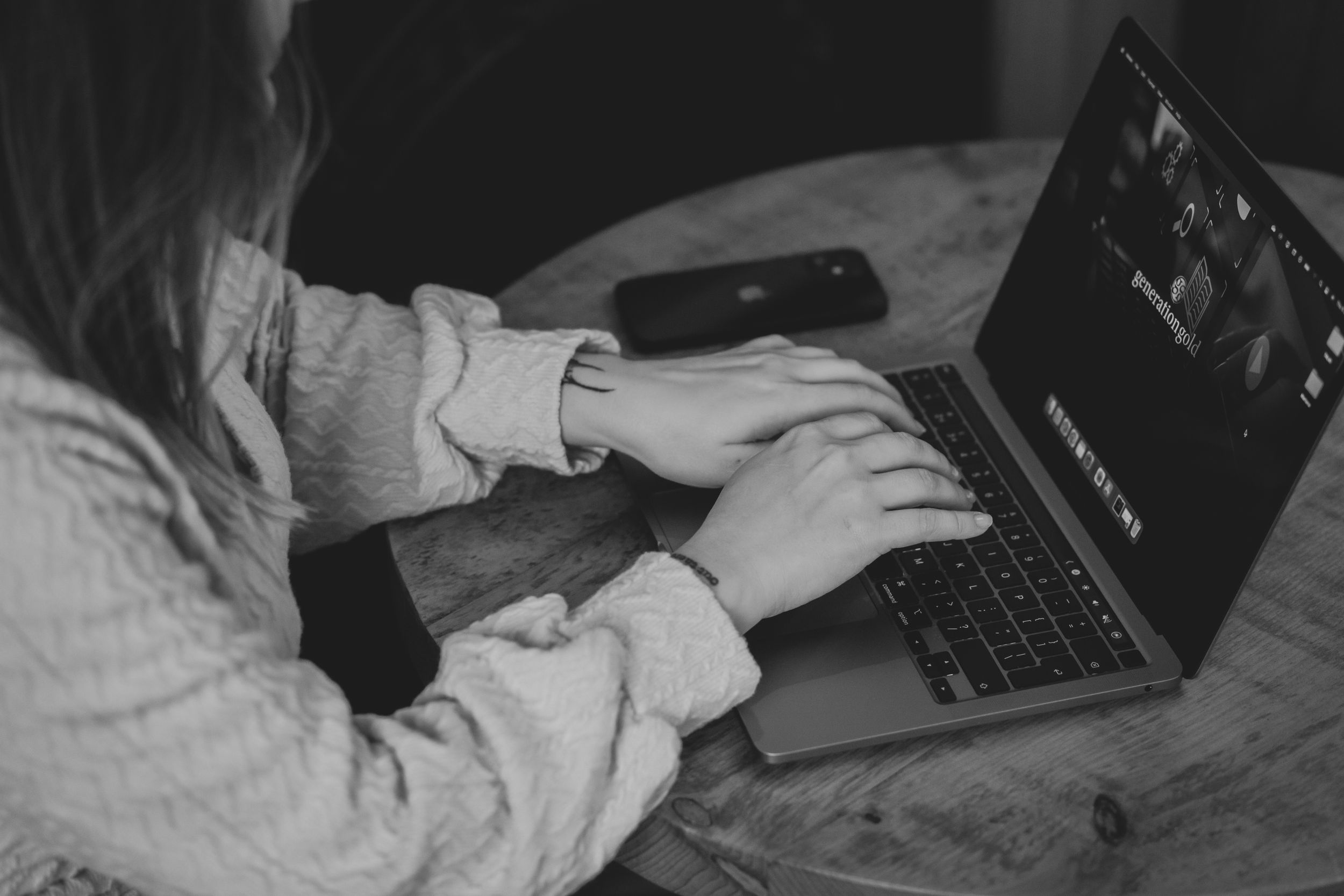 Hands typing on MacBook laptop keyboard in moody black and white lighting.