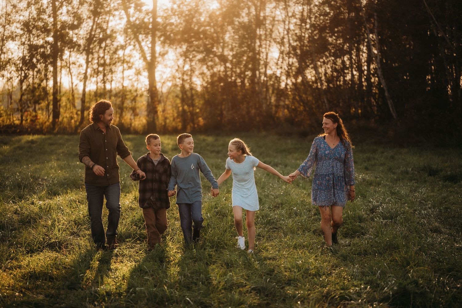 A family runs hand in hand through a sunlit meadow at golden hour.