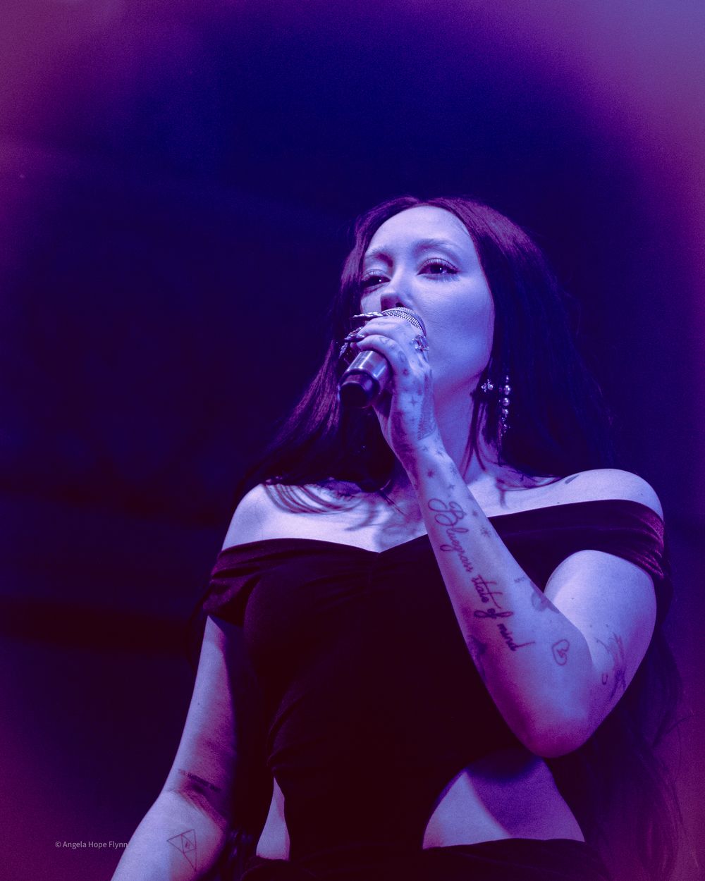 Concert artist performing under purple stage lighting with microphone.