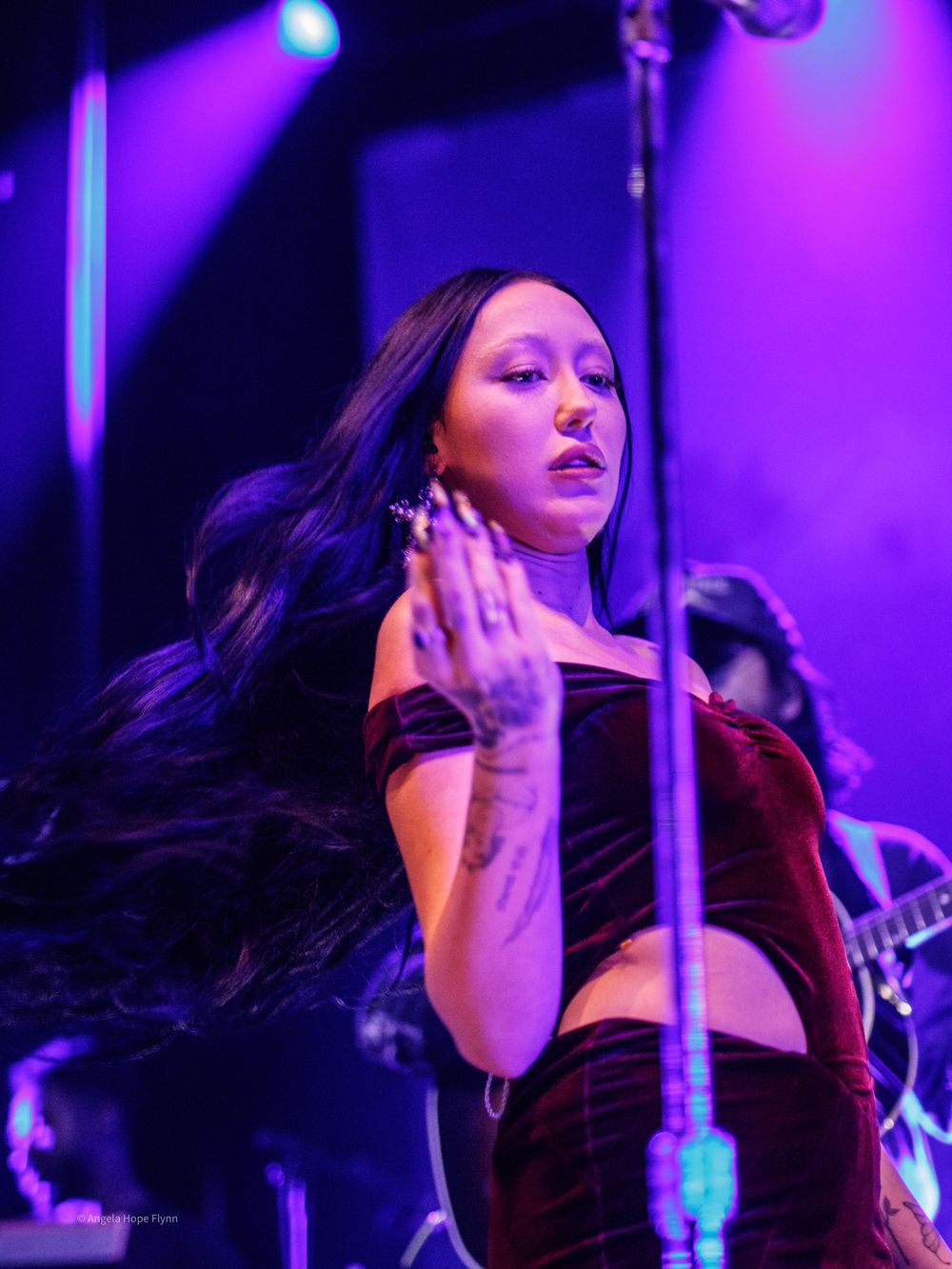 Concert performer in velvet outfit singing on stage with purple lighting effects.