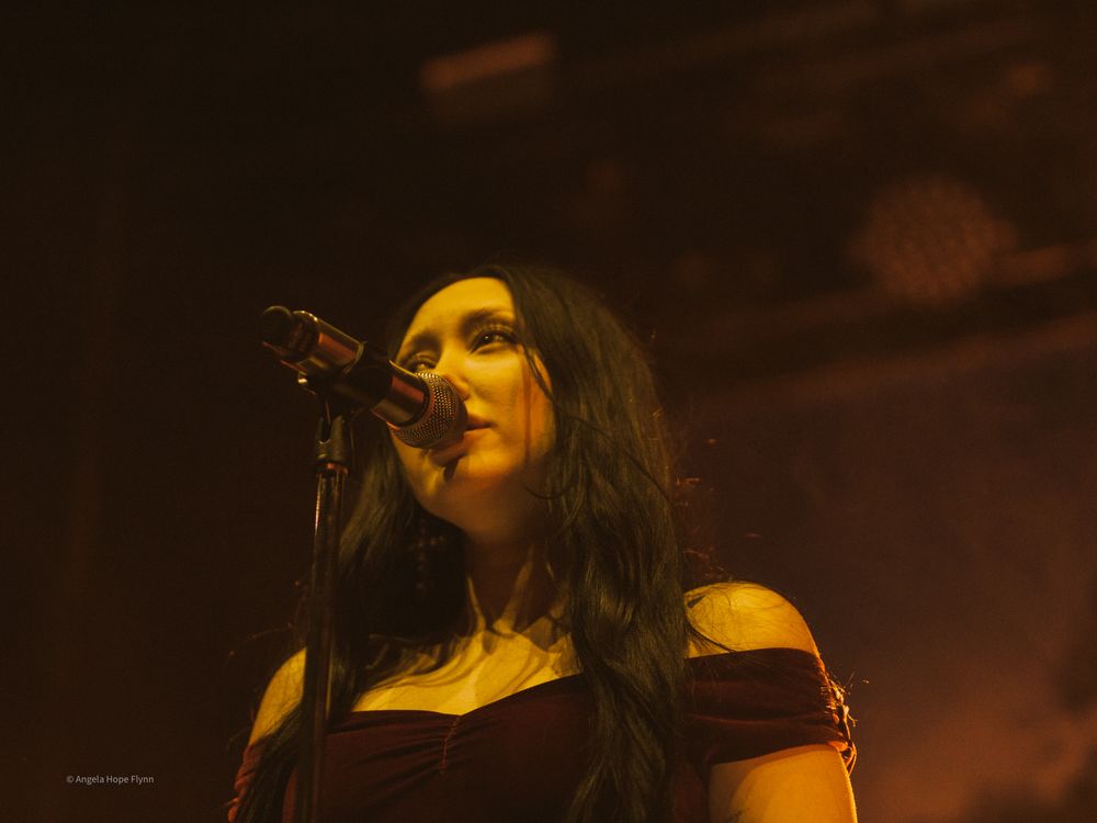 Stage performer singing emotively against warm-toned concert lighting and dark background.