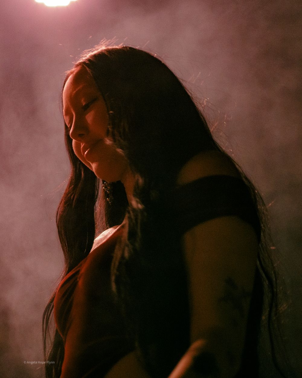 Performance artist singing in atmospheric lighting with smoky background and dramatic side lighting.