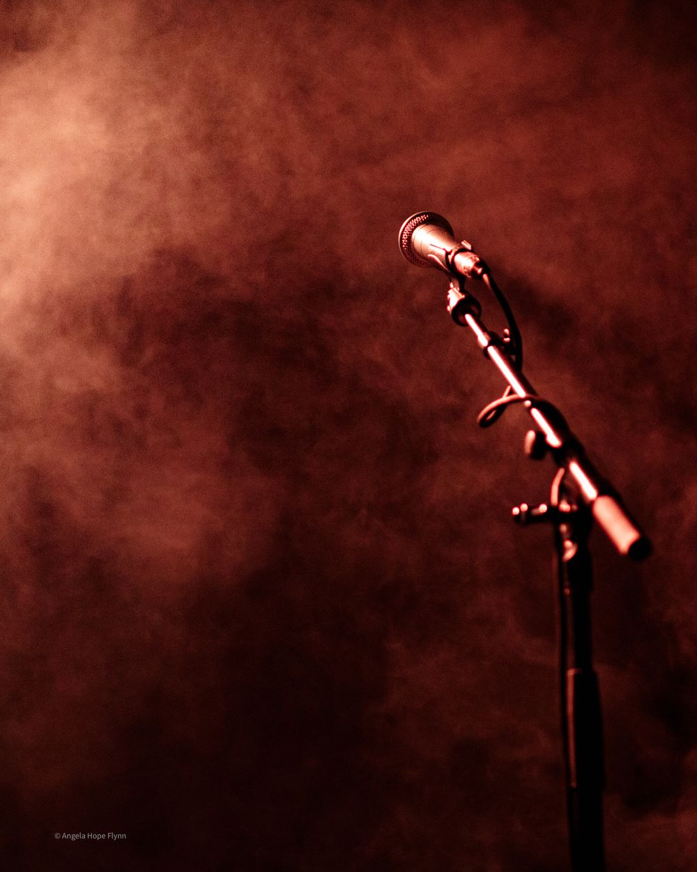 Professional microphone on stand silhouetted against warm red smoky background.