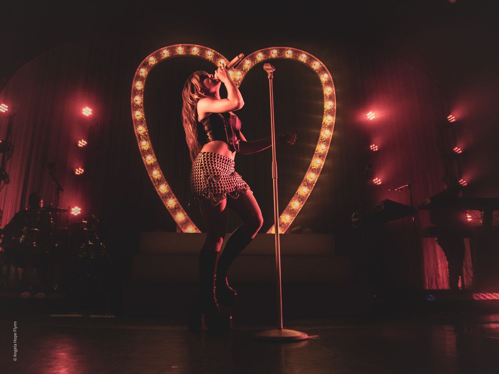 Concert performance with glowing heart-shaped prop and red stage lighting.