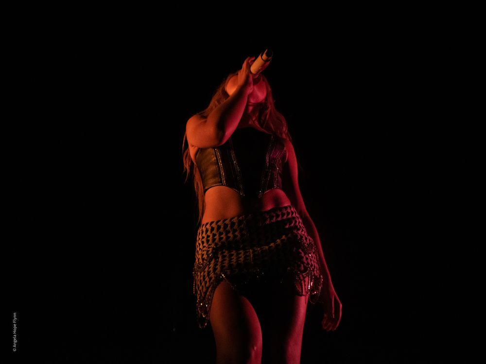 Silhouetted performer in red stage lighting during dramatic concert moment.
