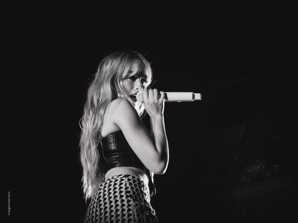 Dramatic black and white performance photo with microphone and stage lighting.