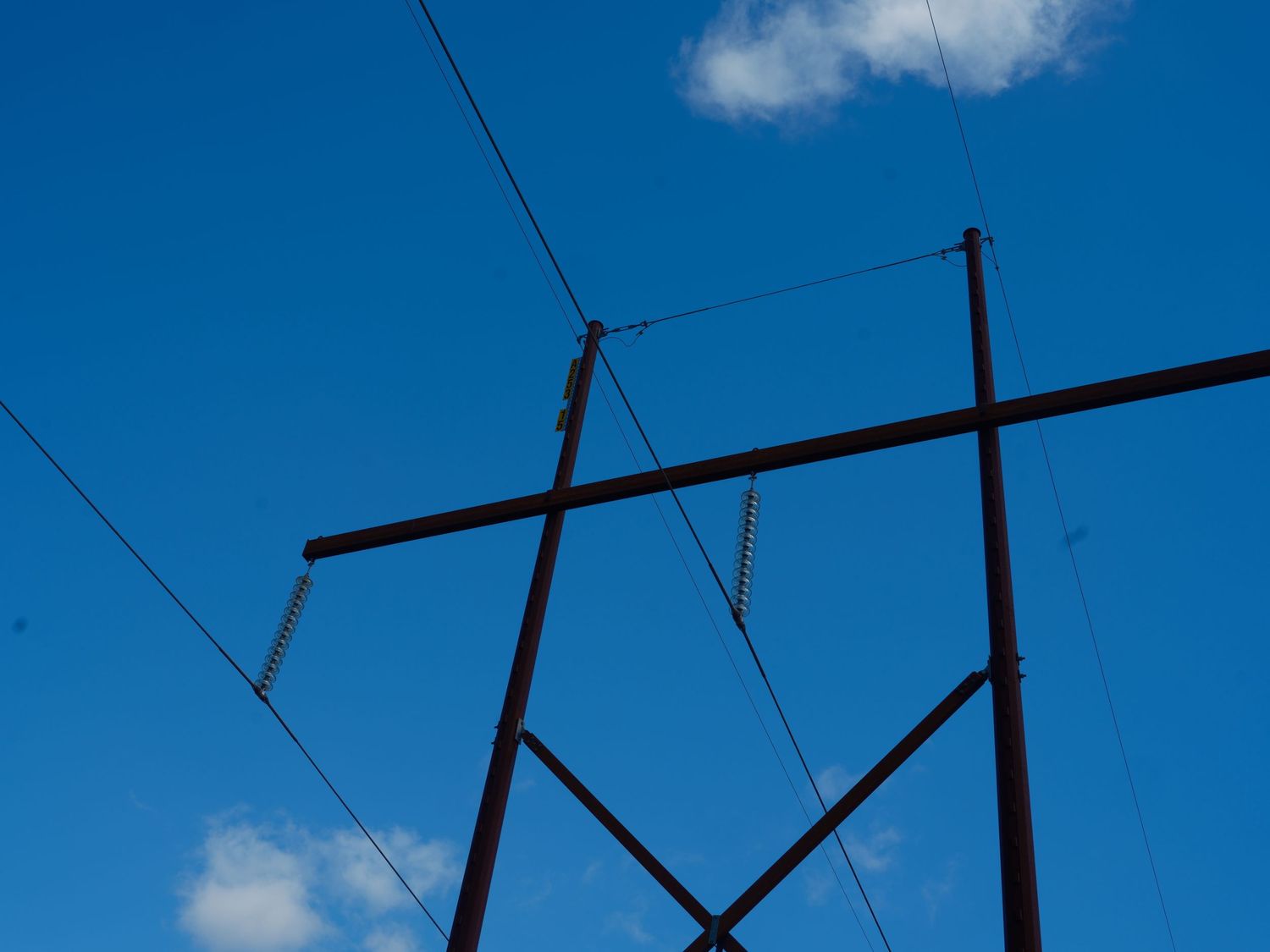 Low angle view of electric power line tower against a vivid blue sky with white clouds.