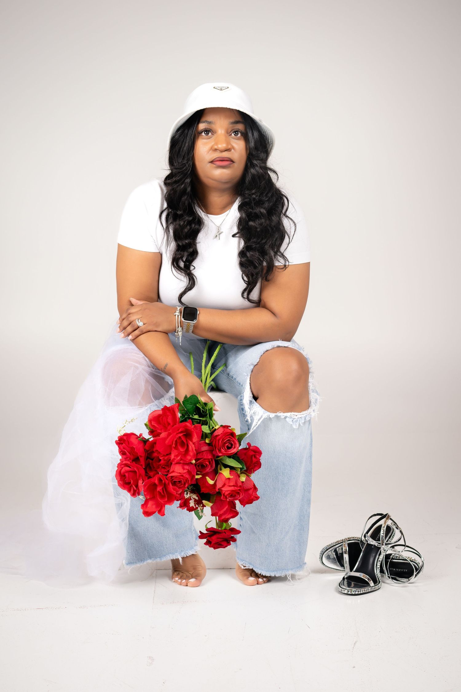 Model in casual attire poses with red roses and sneakers against white background.