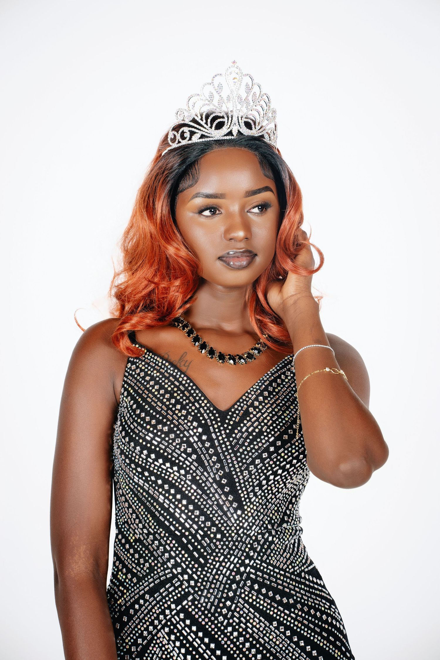 Model wearing a sparkly black dress and tiara poses against white background.