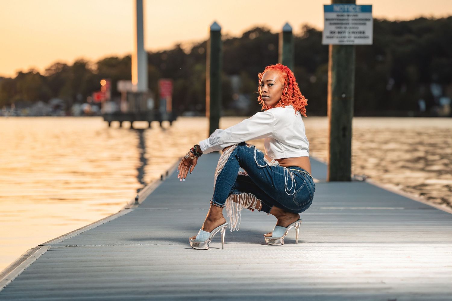 Someone in casual attire sits on a dock during golden hour sunset.