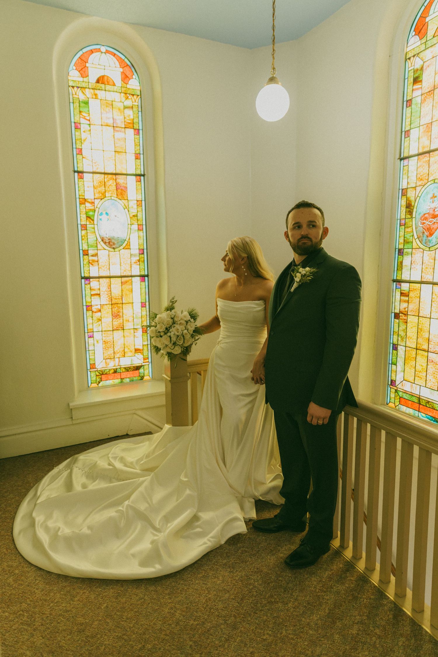 Wedding couple posing in front of stained glass windows in a church.
