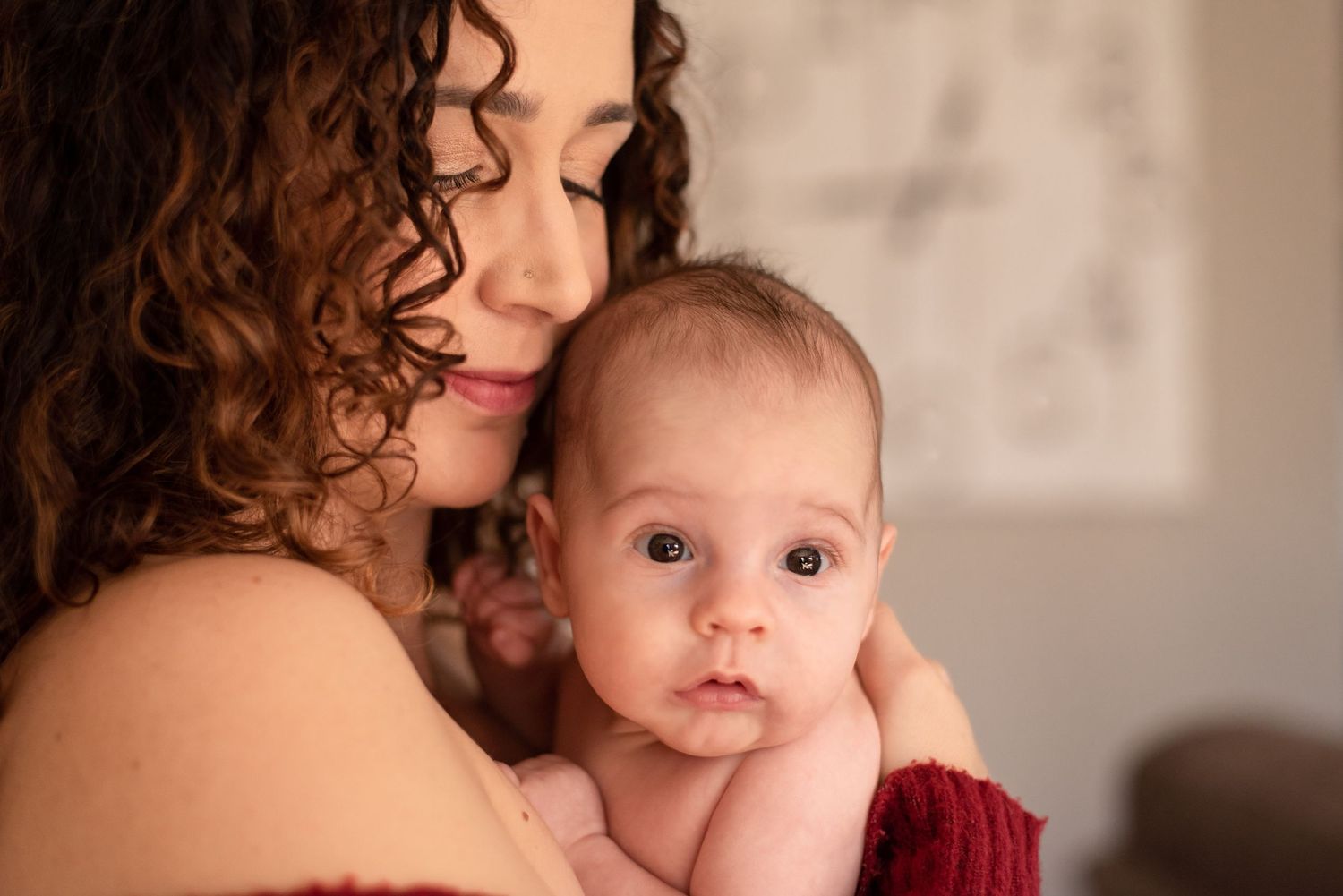 Intimate portrait of tender motherhood moment with curly-haired woman holding baby.