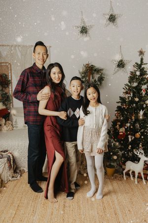 A family poses together in front of a decorated Christmas tree and winter decor in a cozy indoor setting.