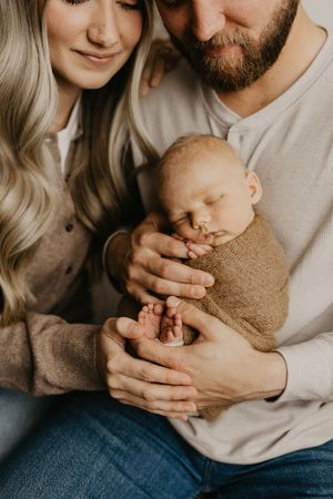 Parents in neutral tones cradle their sleeping newborn baby in a series of intimate portraits.