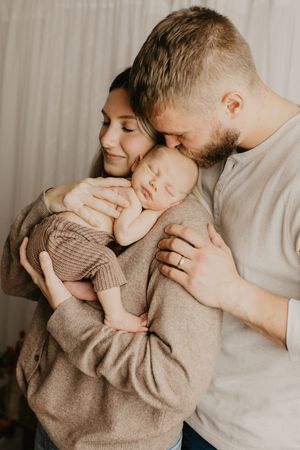 Tender family moments captured in warm tones as parents embrace their baby.