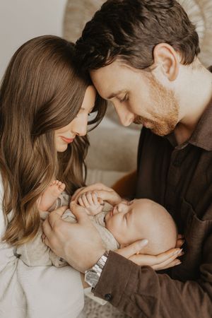A loving couple gazes adoringly at their newborn baby in a warm, intimate family portrait.