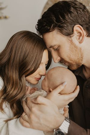 Intimate family portraits showing parents sharing loving moments together with their newborn in soft lighting.