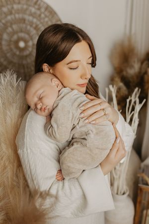 A tender moment captured in soft neutral tones as parent and sleeping baby embrace among dried pampas grass decor.