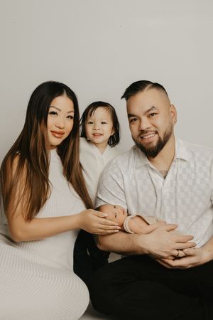A family wearing white and black outfits poses together in a minimalist studio setting for intimate portraits.