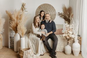 A family poses together against a neutral backdrop with boho decor including pampas grass and woven wall art.