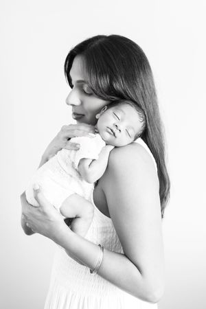 Black and white photo of a mother tenderly holding her sleeping newborn baby against her chest.