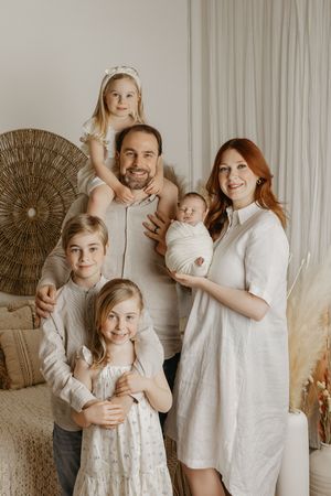 Happy family of six posing together, parents with four children including a newborn baby, in a cozy neutral-toned room.