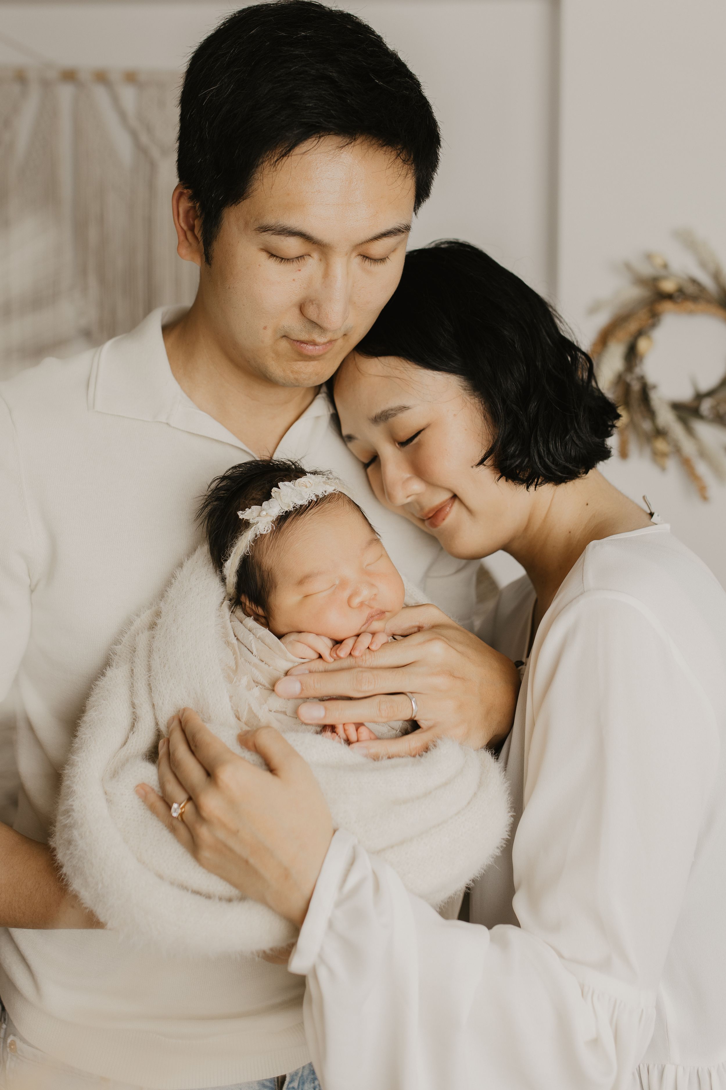 Warm family portrait series in white showing gentle moments with sleeping infant.