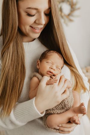Intimate newborn photography session with soft white sweater and natural lighting.