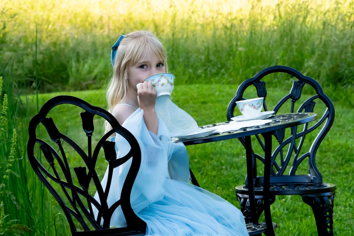 Person in blue dress having tea at outdoor garden table.