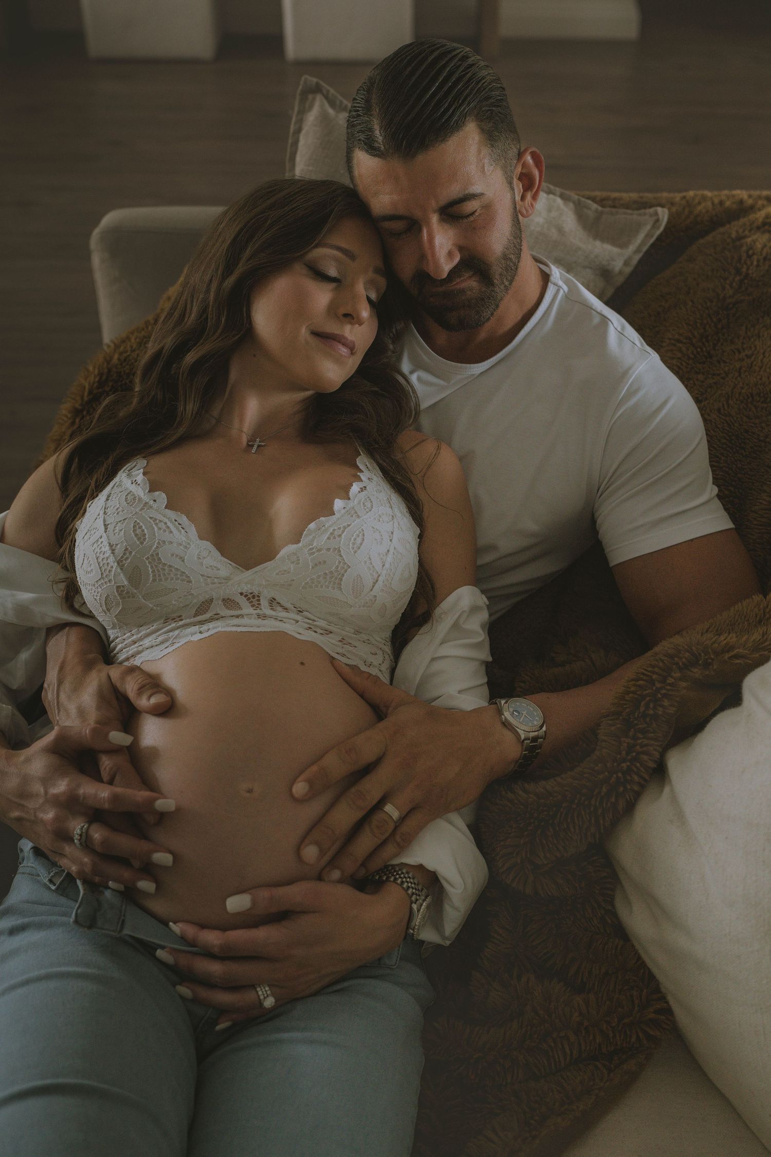 Intimate indoor maternity moment on couch with white lace top.