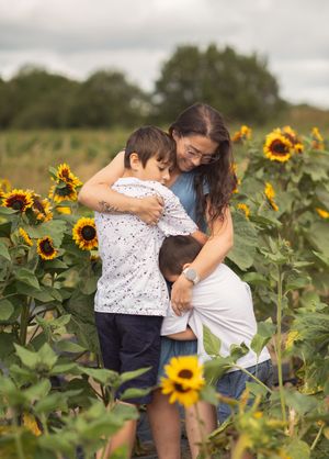 A mother embracing her two sons whilst stood arouns sunflowers