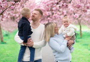 A family shares a happy moment together under blooming pink cherry blossom trees in a spring garden.