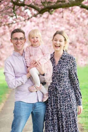 Family enjoying spring day under blooming pink cherry blossoms in park.