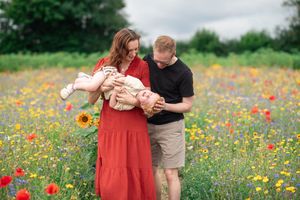 Parents play with their son in a flower field.