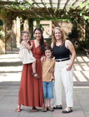 A family stands together in a shaded outdoor courtyard wearing coordinated rust and neutral colored outfits.