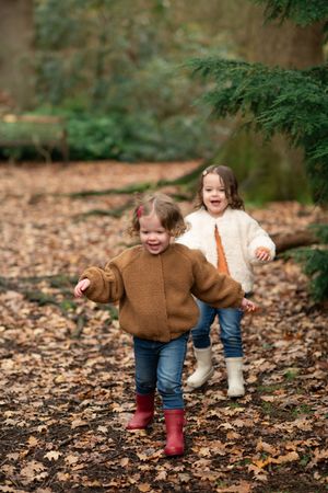 Two children run and play together through fallen autumn leaves in a forest setting.