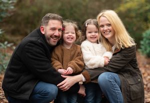 A family sits together outdoors on fallen autumn leaves sharing joyful moments during a photo session.
