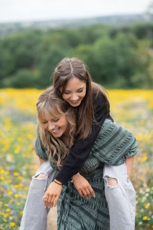 A mother gives her daugther a piggy back in a yellow flower field.