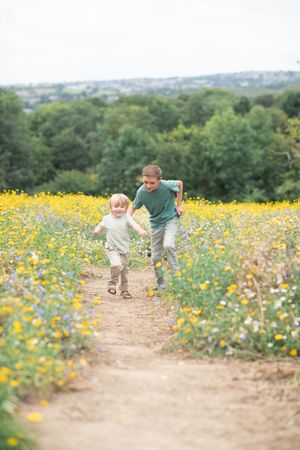 Two brothers run together in a yellow flower field.