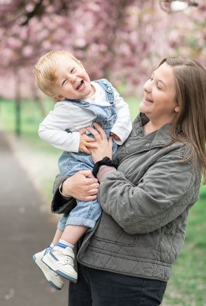 A mother tickles her young son under the cherry blossom trees.