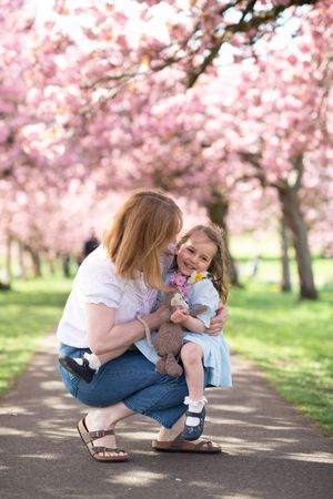 A mother and daugther cuddling under cherry blossom trees