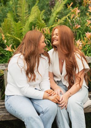 Two adult sisters sat on a bench laughing together