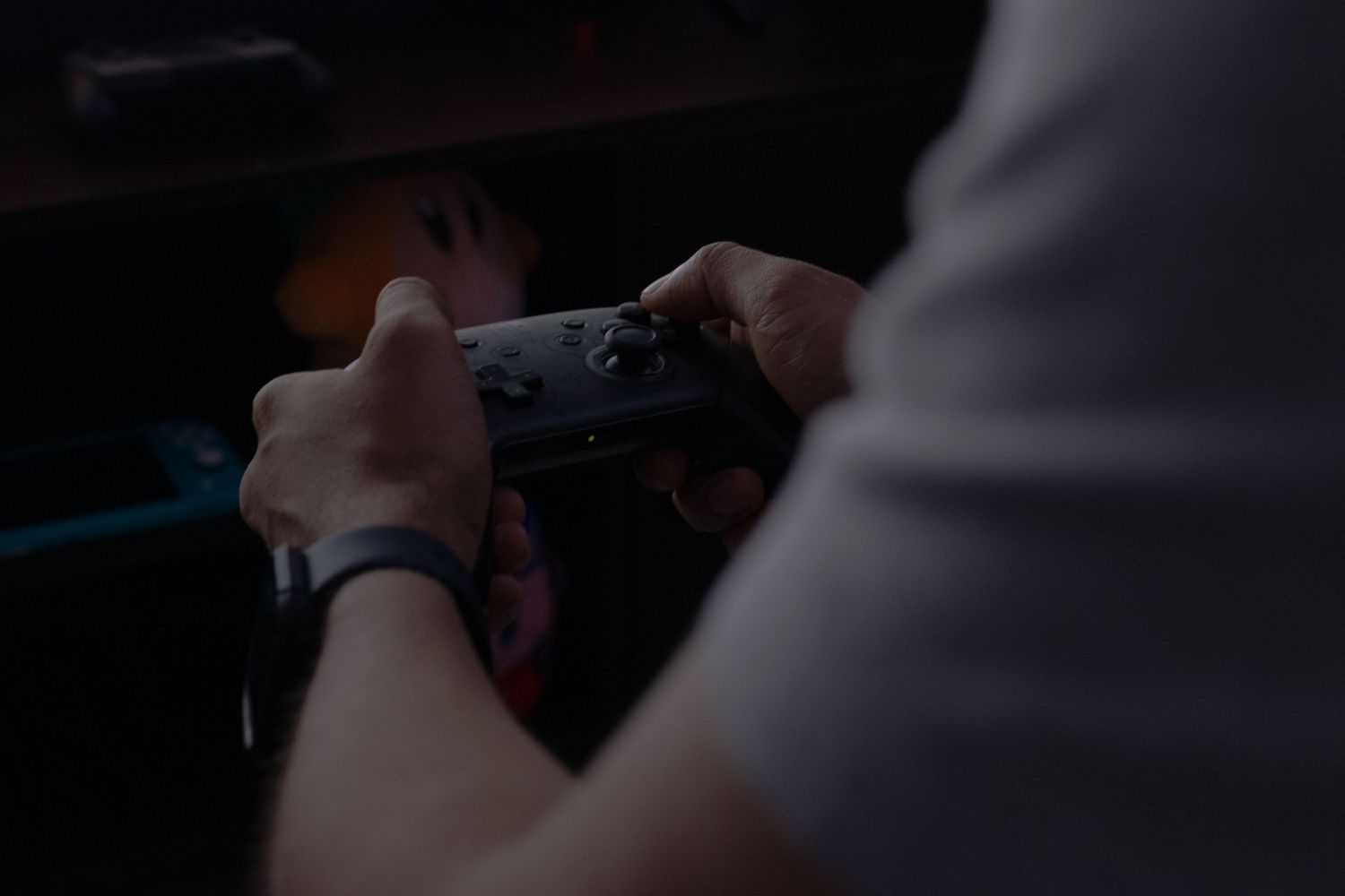 Hands holding a video game controller in a dimly lit room.